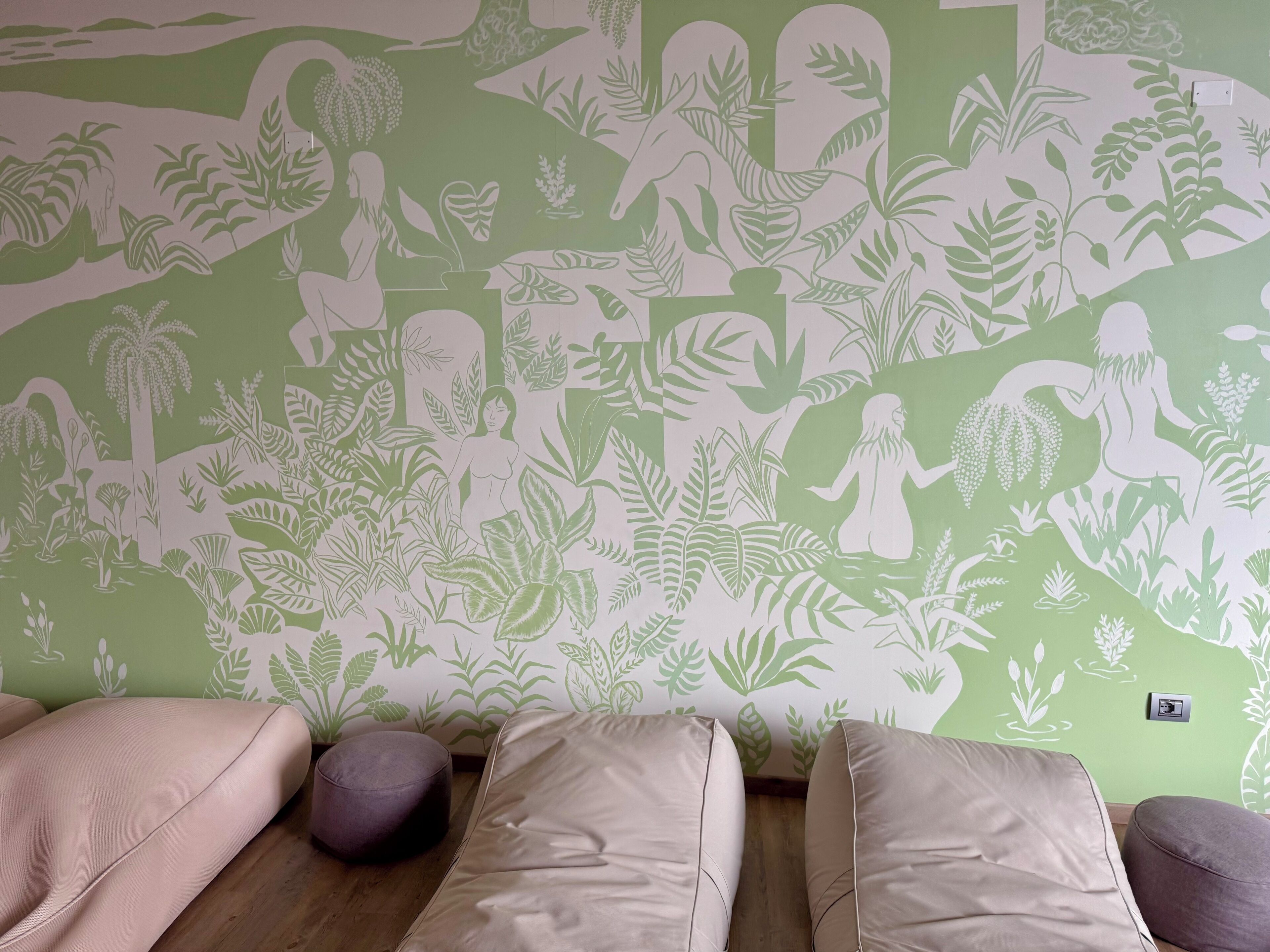 Una stanza con carta da parati verde e decorata con foglie, pavimento in legno e tre divani beige.