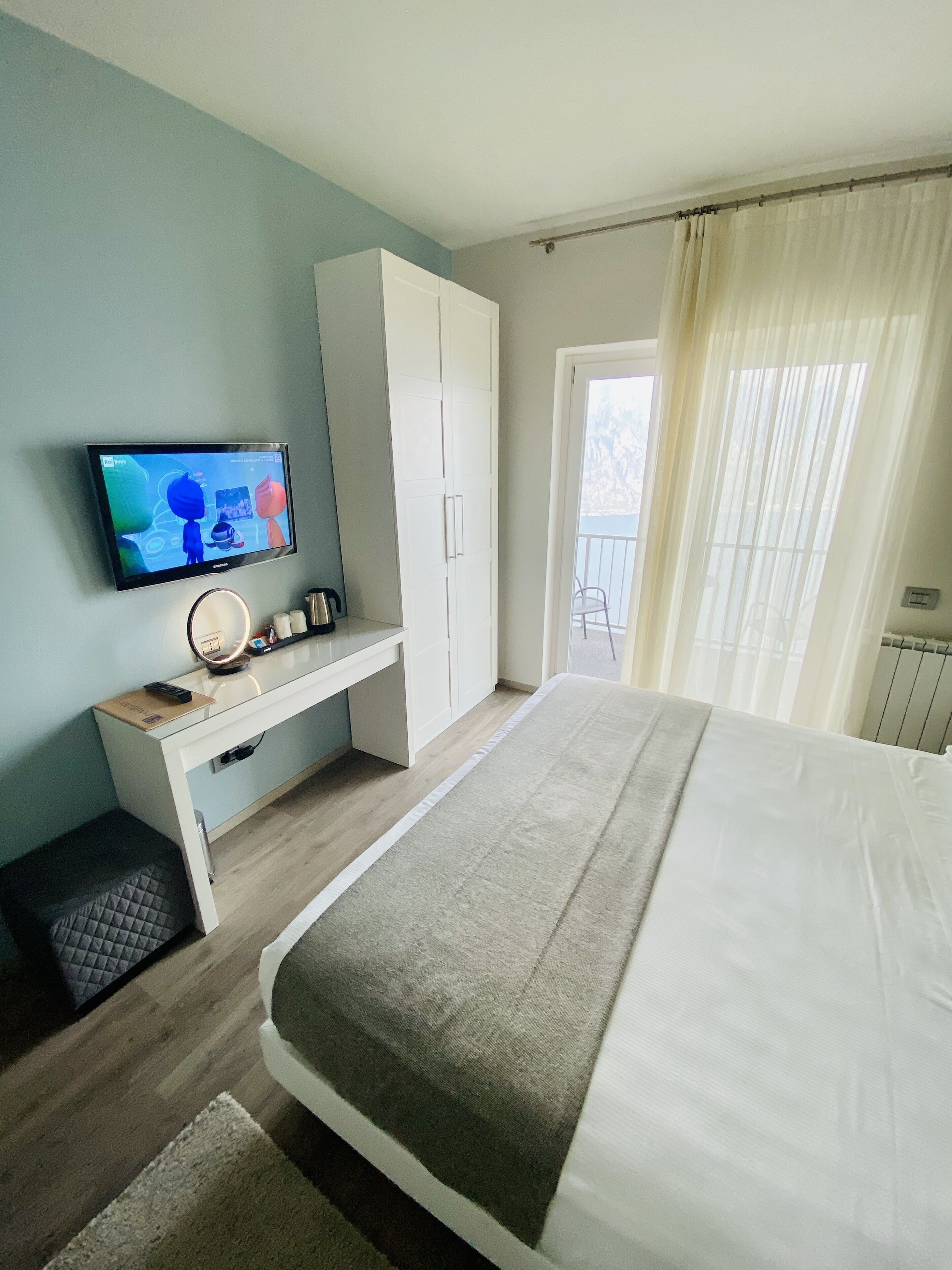 A bedroom with a bed, a desk with a computer, a television, and a window with curtains.