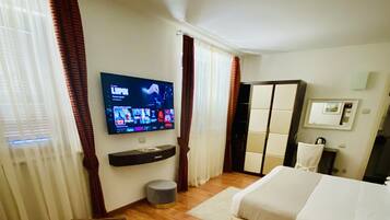 A hotel room with a bed, a TV mounted on the wall, a small table, and a wardrobe.
