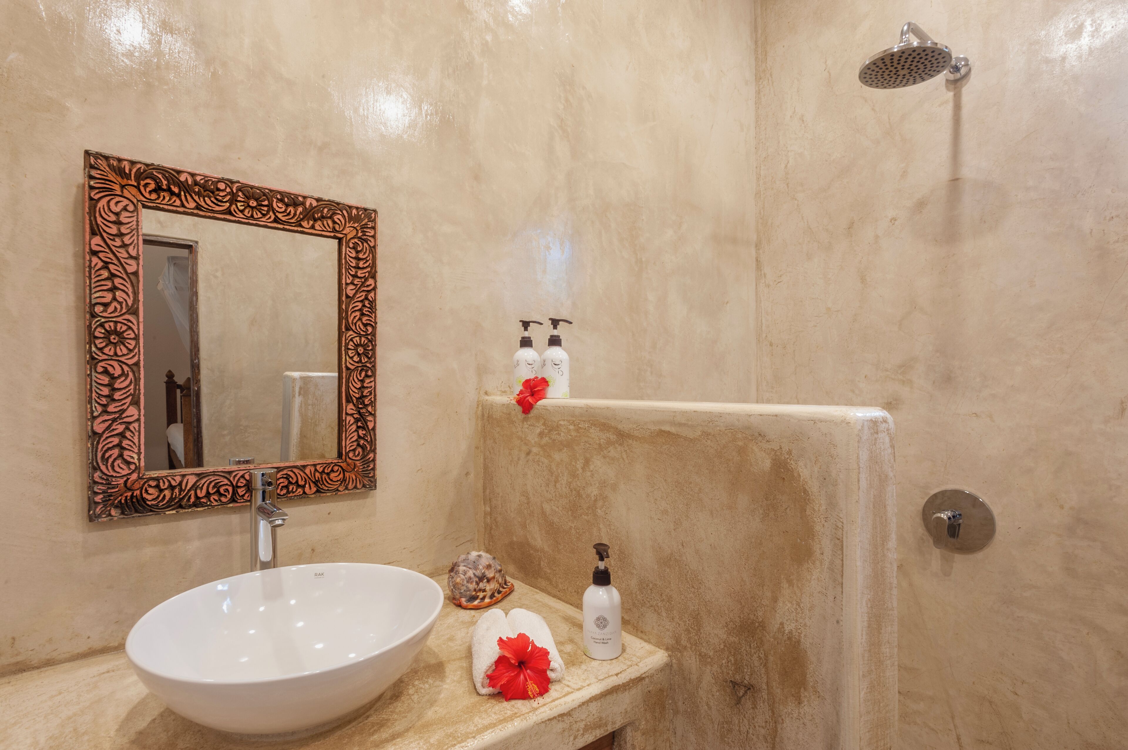 Un bagno con un lavandino bianco, uno specchio con cornice decorata, un soffione doccia a mano e articoli da toilette sul ripiano.