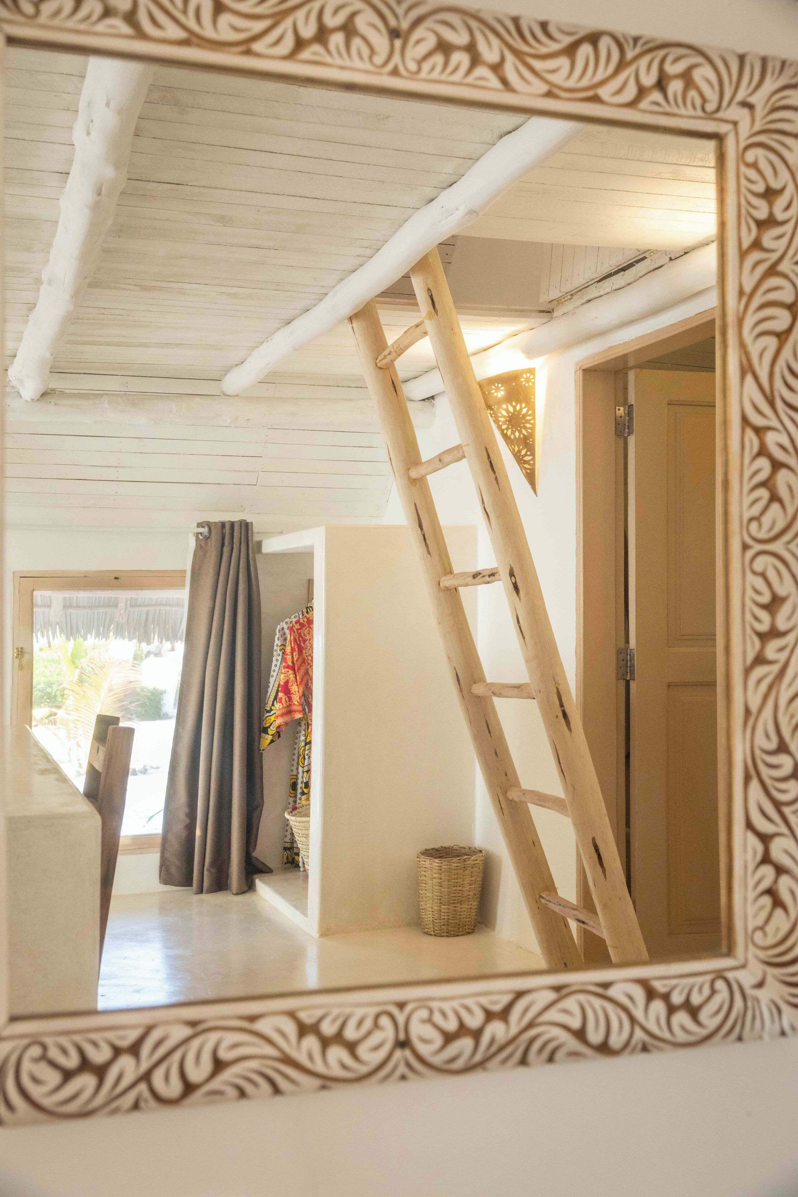 A room with a wooden ceiling, a ladder, a door, and a curtain.