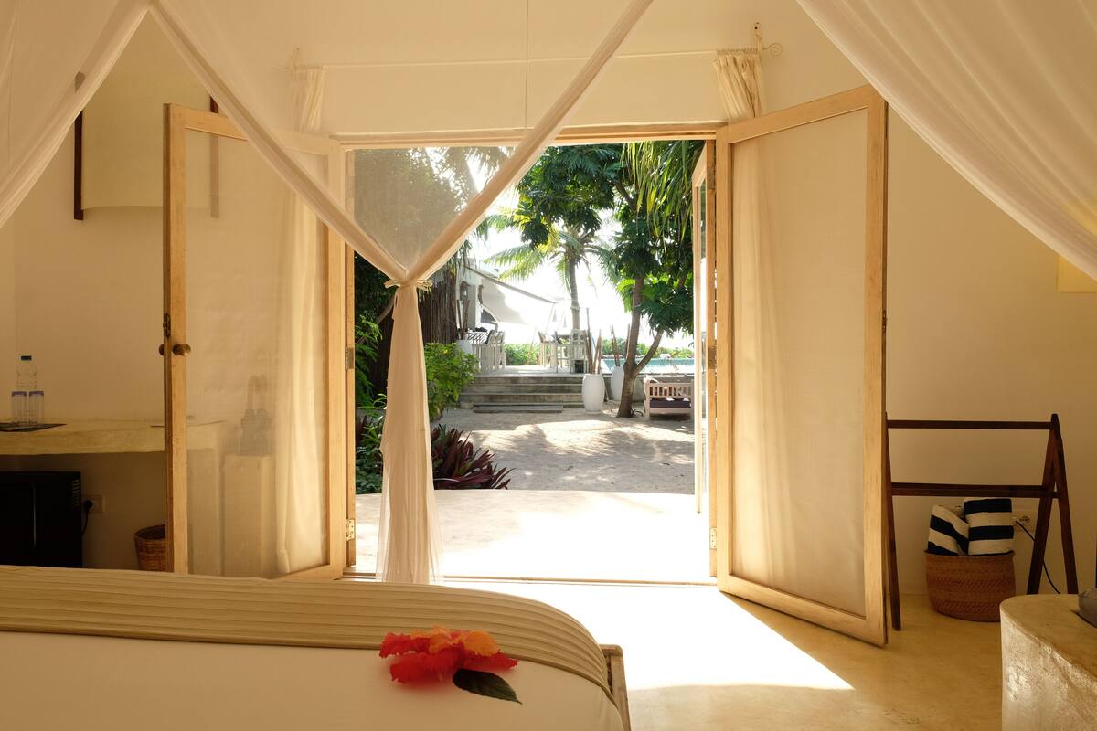 Una habitación con una cama, una ventana con cortinas, una escalera de madera y vistas a un jardín y escalones afuera.