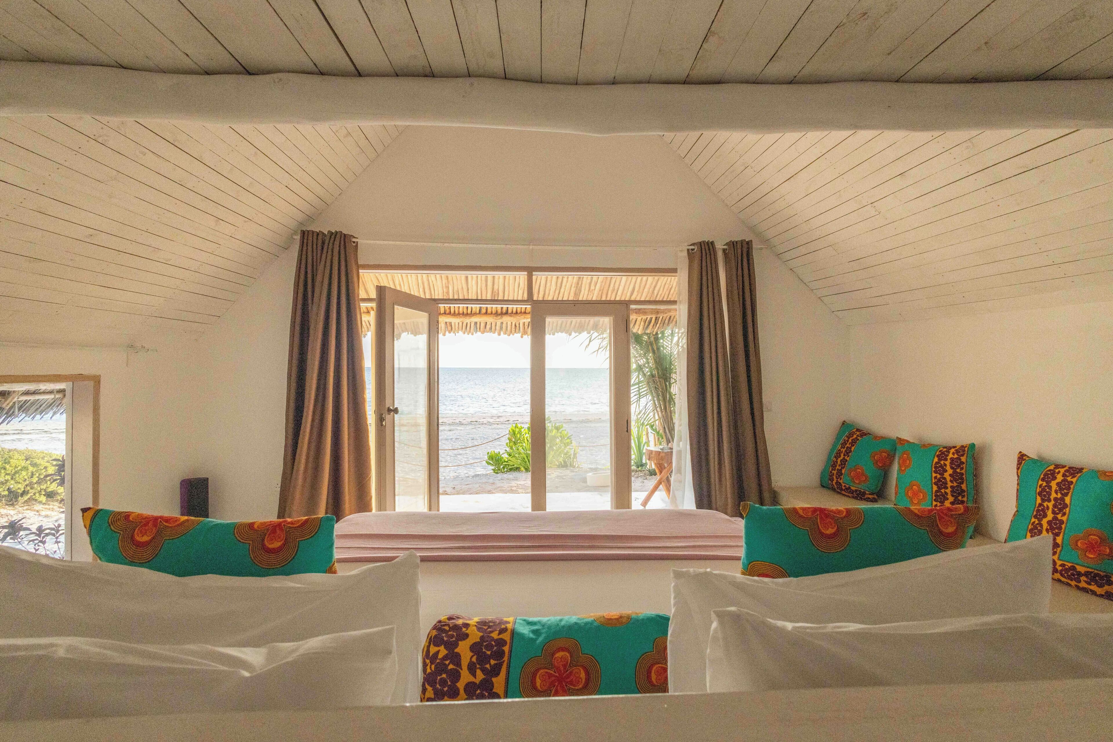 Un dormitorio con un ventanal grande, una cama con almohadas coloridas y vista al mar.
