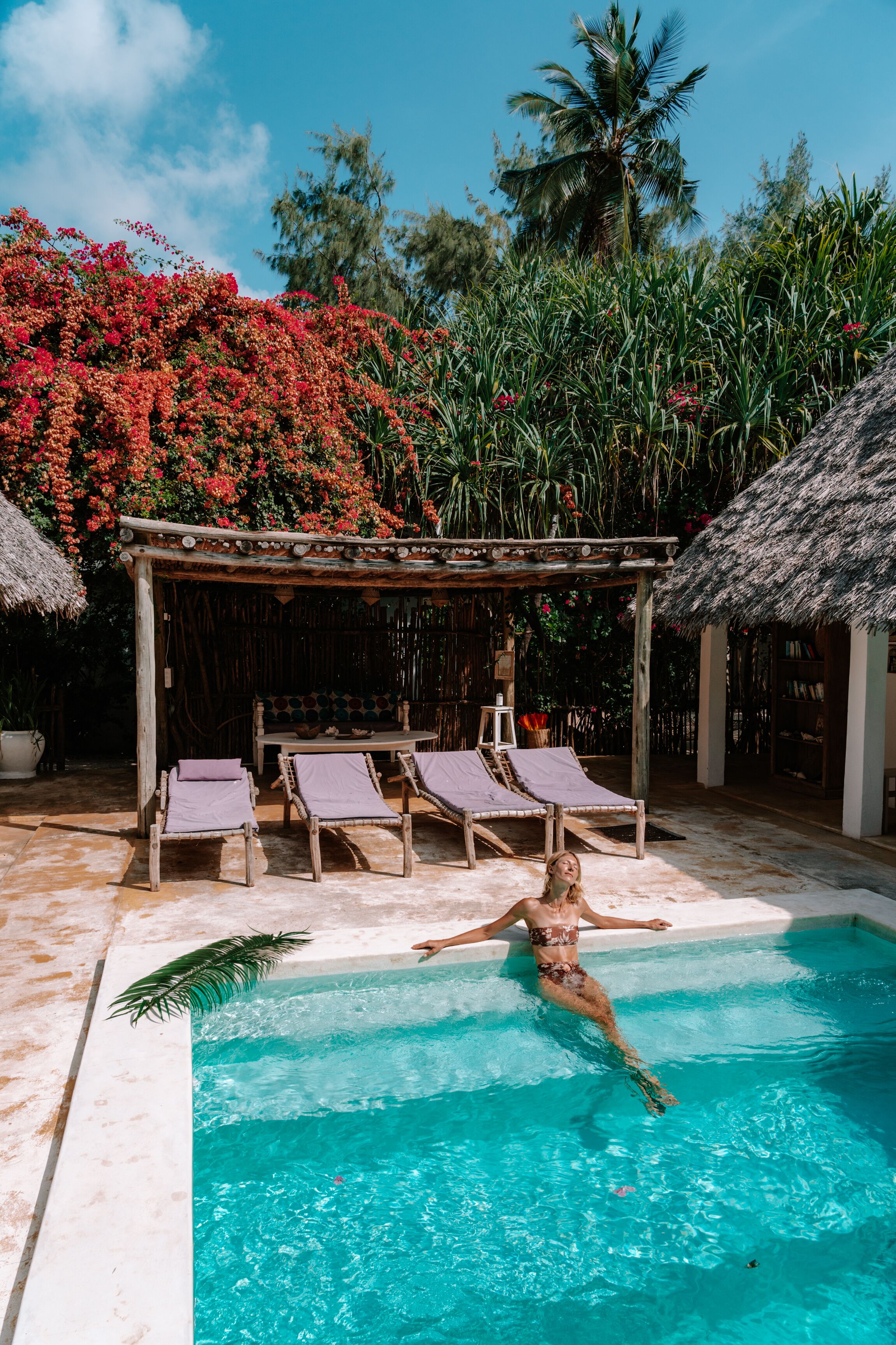 A pool area with lounge chairs, a thatched-roof structure, and lush greenery.