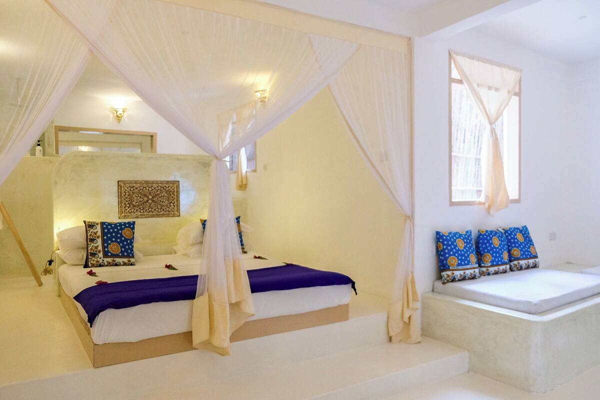 Un dormitorio con cama con dosel, una zona de estar con cojines y un adorno de pared.
