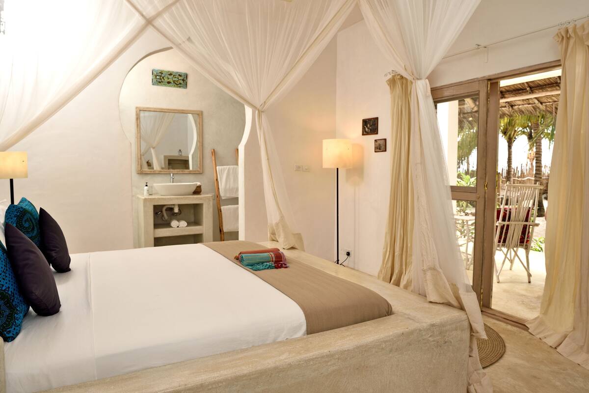 Un dormitorio con cama, mesita de noche, lámpara y vistas al exterior.