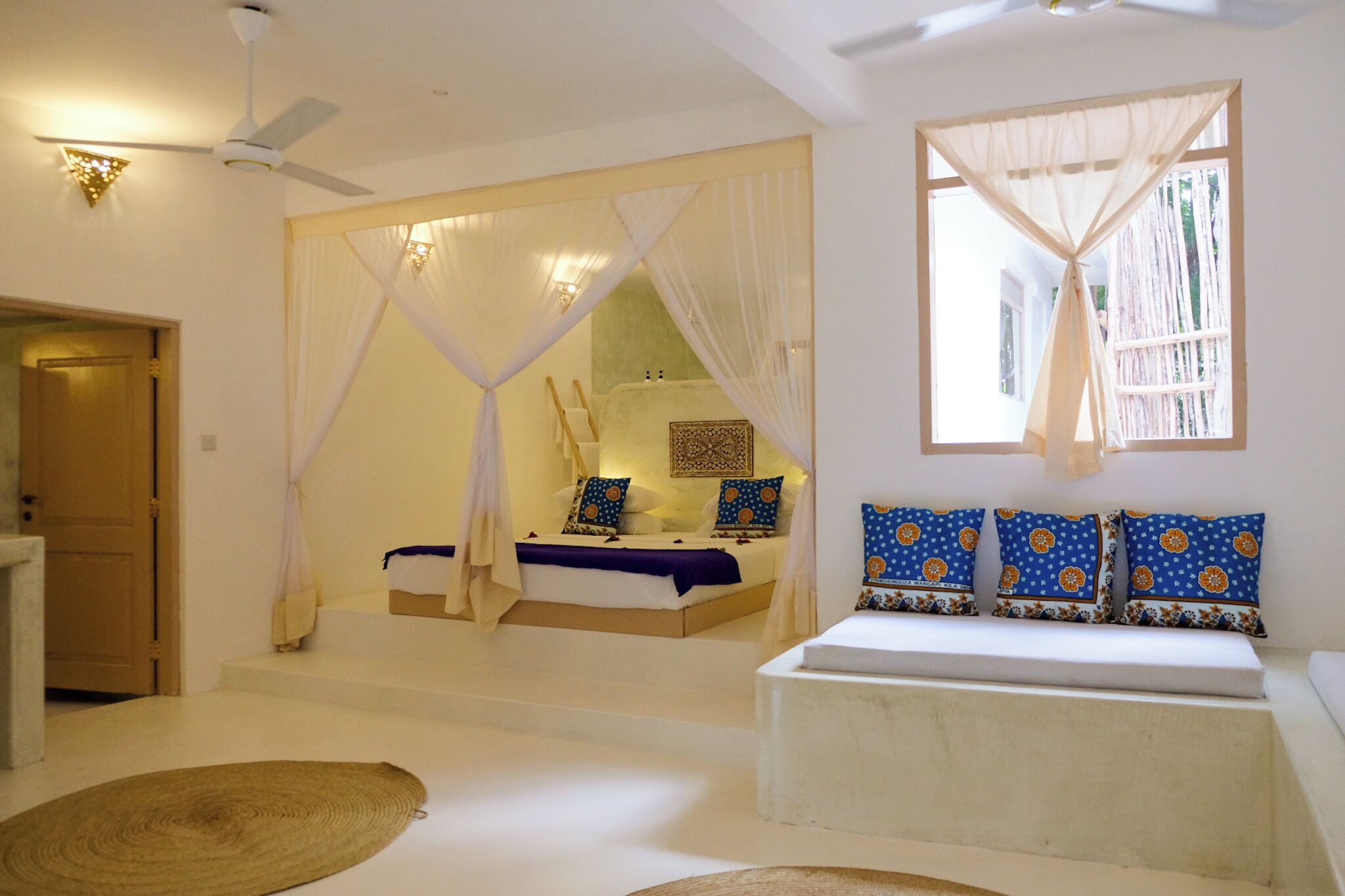 A bedroom with a bed, a bench, a ceiling fan, and a window with curtains.