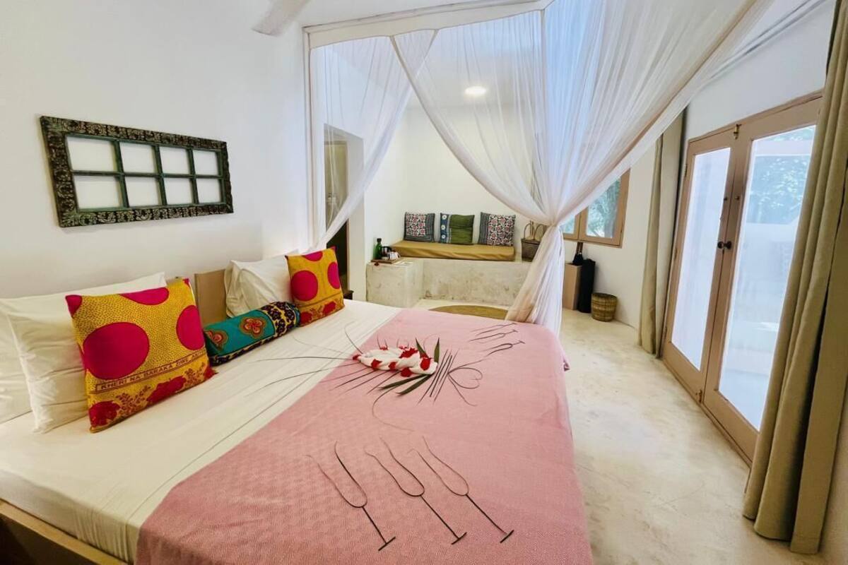 Un dormitorio con cama, ventilador de techo, ventana con cortinas y mesita de noche.