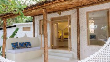 Ein gemütlicher Sitzbereich im Freien mit einer Holz-Pergola, einer weißen Wand mit Struktur und einem großen Fenster.