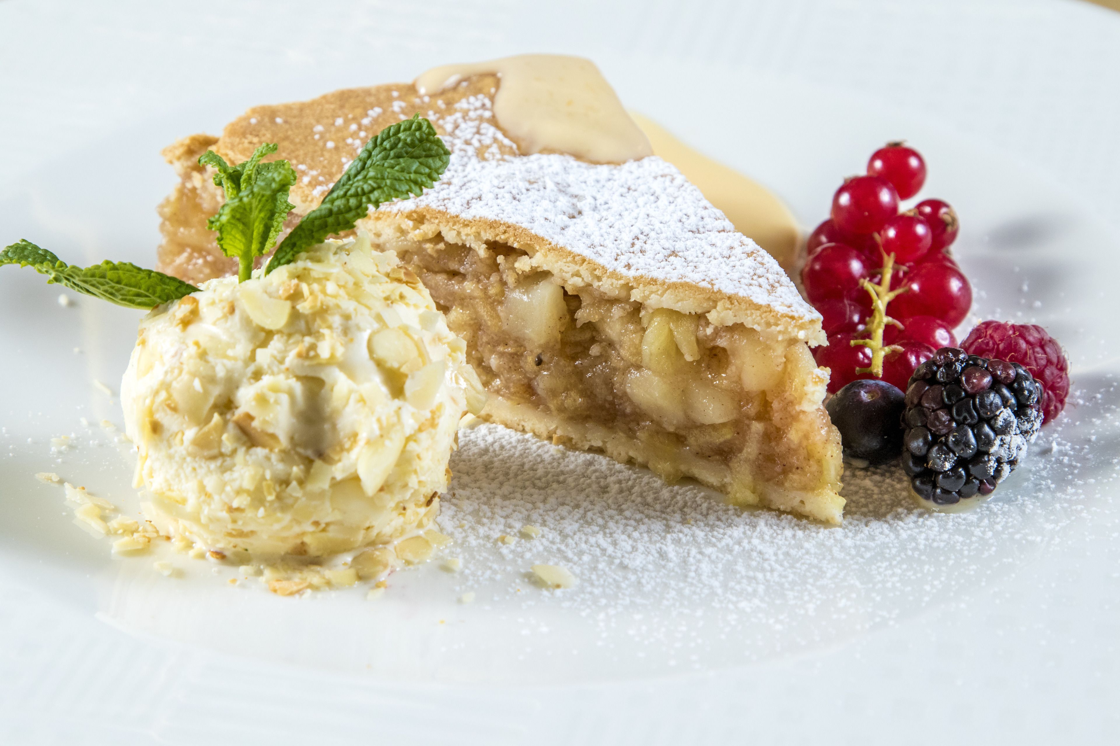 A dessert plate with a slice of apple pie, a scoop of vanilla ice cream, and fresh berries.