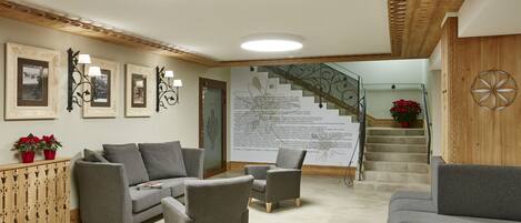 A modern lobby with a grey sofa set, wooden accents, and a staircase with a decorative wall.