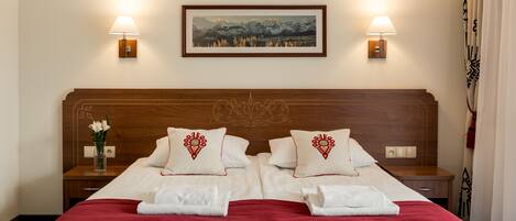 A hotel room with a large bed, two bedside tables, a nightstand with a vase of flowers, and two wall-mounted lamps.