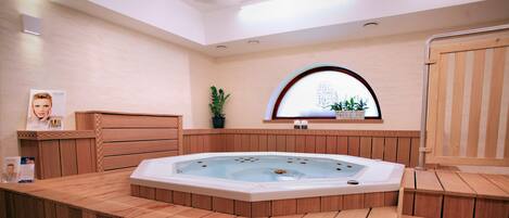 Un espacio tipo spa de madera con un jacuzzi, bancos de madera, una planta en maceta y un ventanal con vistas.