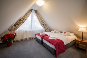 Quarto com uma cama grande, duas mesas de cabeceira, luminária, um vaso com planta e janela com cortinas.