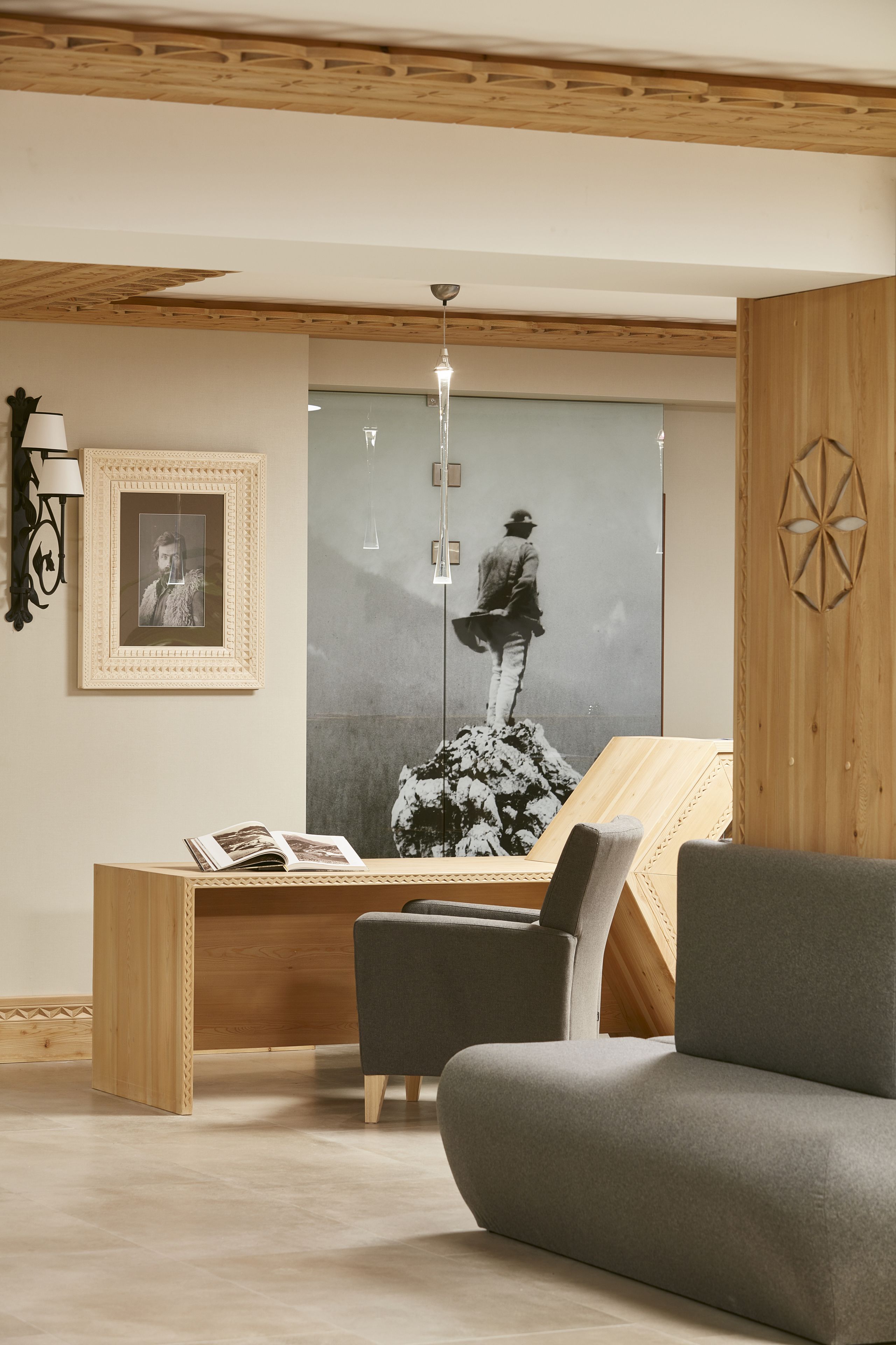 A modern living room with a wooden ceiling, a large framed photograph, a reading area with a magazine, and a grey sofa.