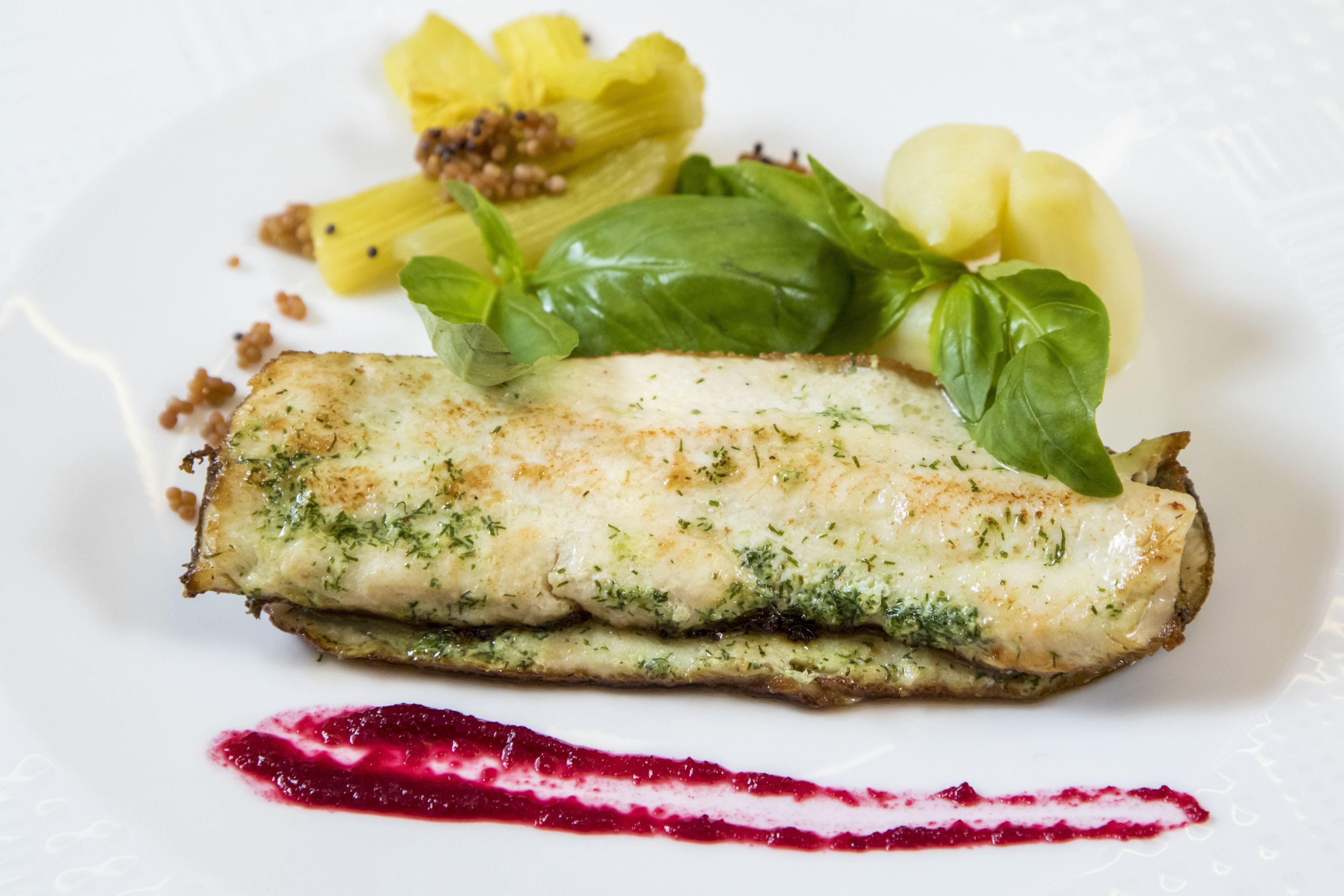 A plate with a fish fillet, green sauce, and a red sauce.