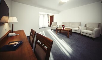 Uma sala de estar com uma mesa de madeira, duas cadeiras, um sofá e uma mesinha de centro.