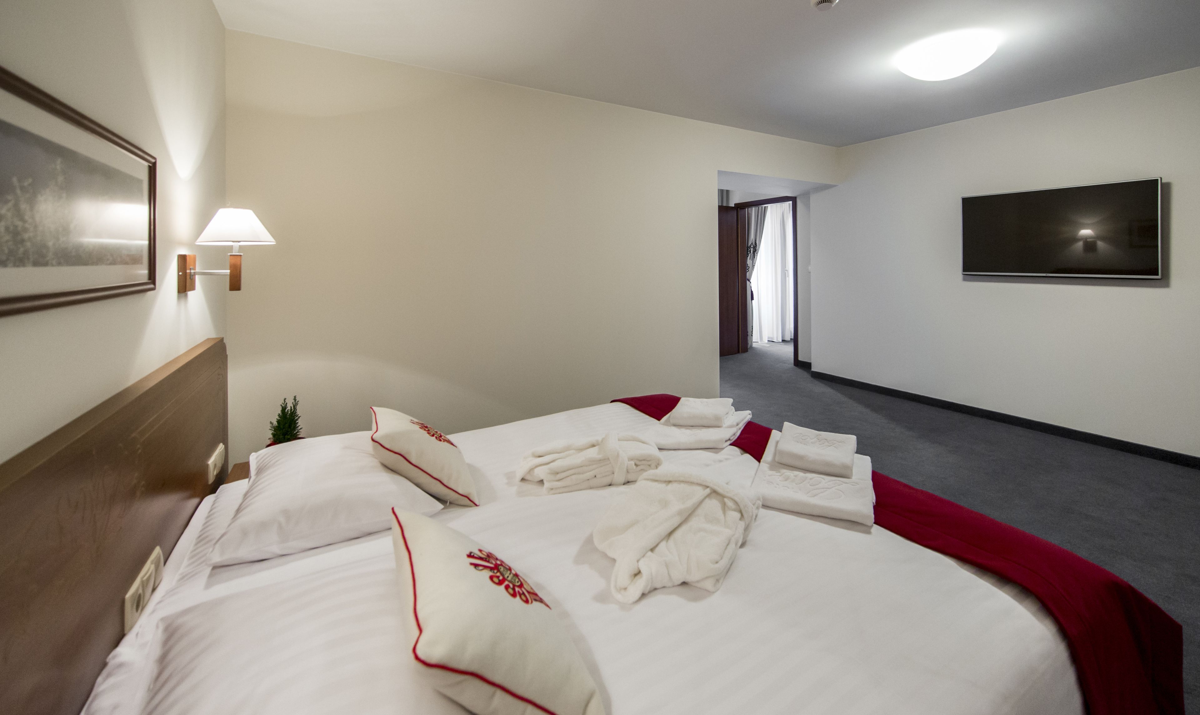 Una habitación de hotel con una cama bien hecha, un televisor en la pared y un pasillo que conduce a otra habitación.