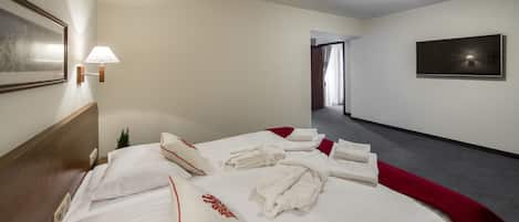 Una habitación de hotel con una cama bien hecha, un televisor en la pared y un pasillo que conduce a otra habitación.