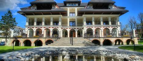 A large, multi-story building with a symmetrical facade, multiple balconies, and a central entrance with steps leading up to it.
