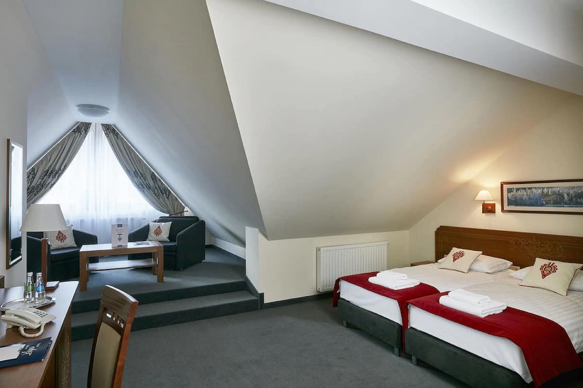 Quarto de hotel com duas camas, uma escrivaninha, uma cadeira, um sofá e uma escada.