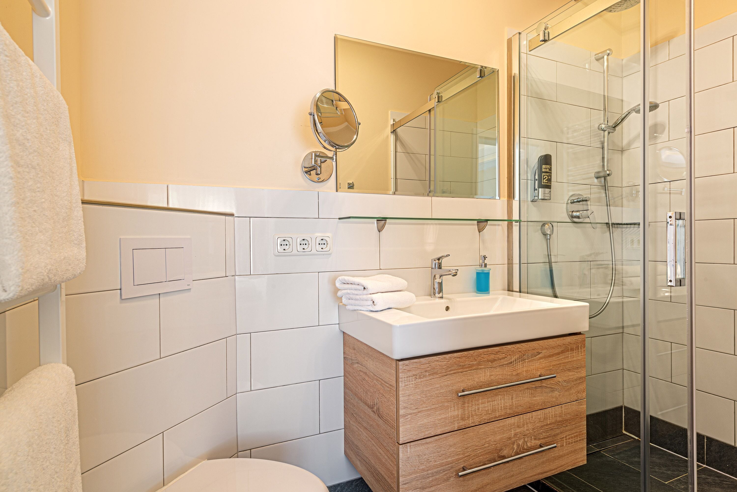 A modern bathroom with a glass shower enclosure, a wooden vanity with a white sink, and a mirror above the vanity.