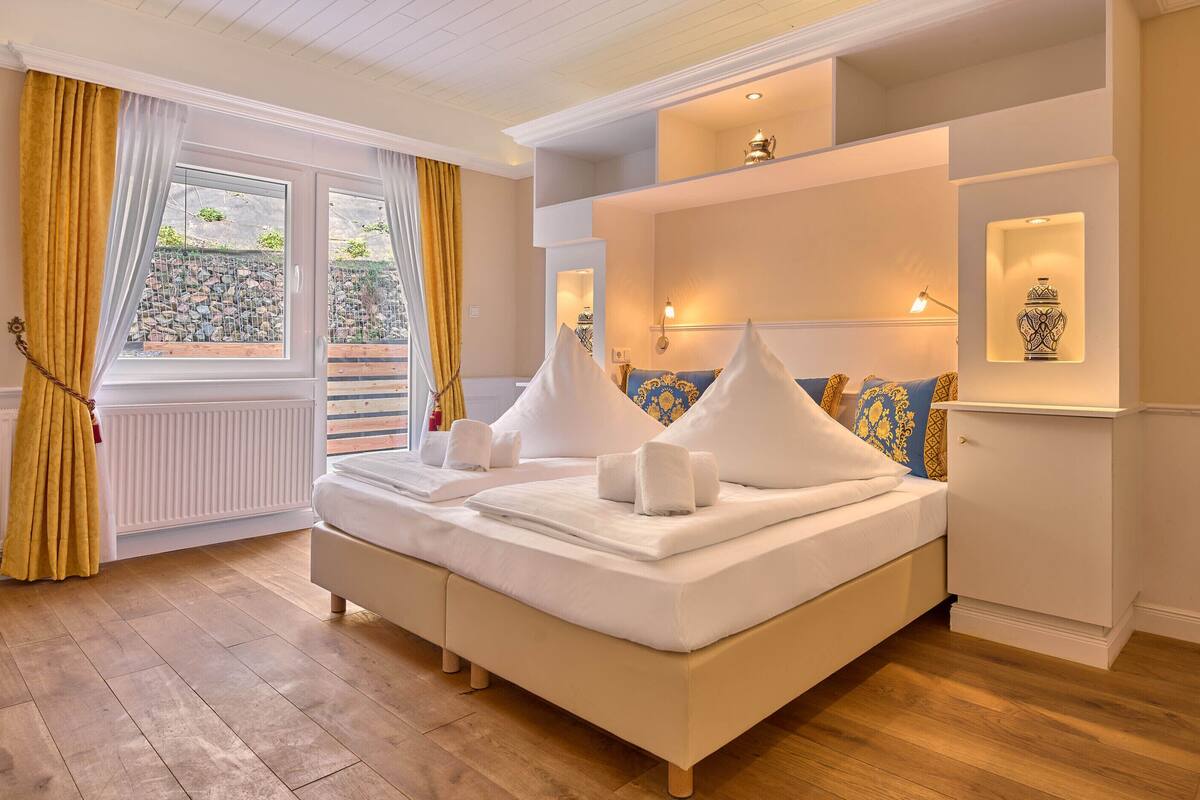 Une chambre bien éclairée, avec un grand lit, une fenêtre avec des rideaux et une vue sur l’extérieur.