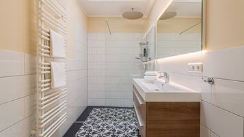 Een moderne badkamer met een vloer van witte tegels, een houten wastafelmeubel, een douchecabine van glas en een dakraam.