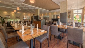 Ein Restaurant mit Holztischen und grau gepolsterten Stühlen, das sich durch eine karierte Decke und Pendelleuchten auszeichnet.