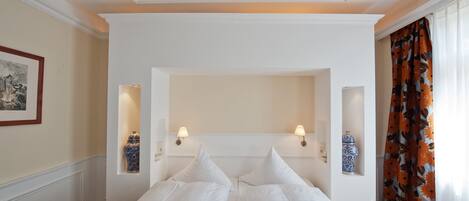 Una camera d'albergo con un letto grande, due lampade a parete, un quadro incorniciato e una finestra con tende.