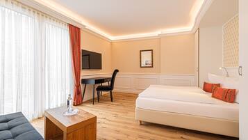A hotel room with a bed, a desk, a chair, a TV, and a window with curtains.