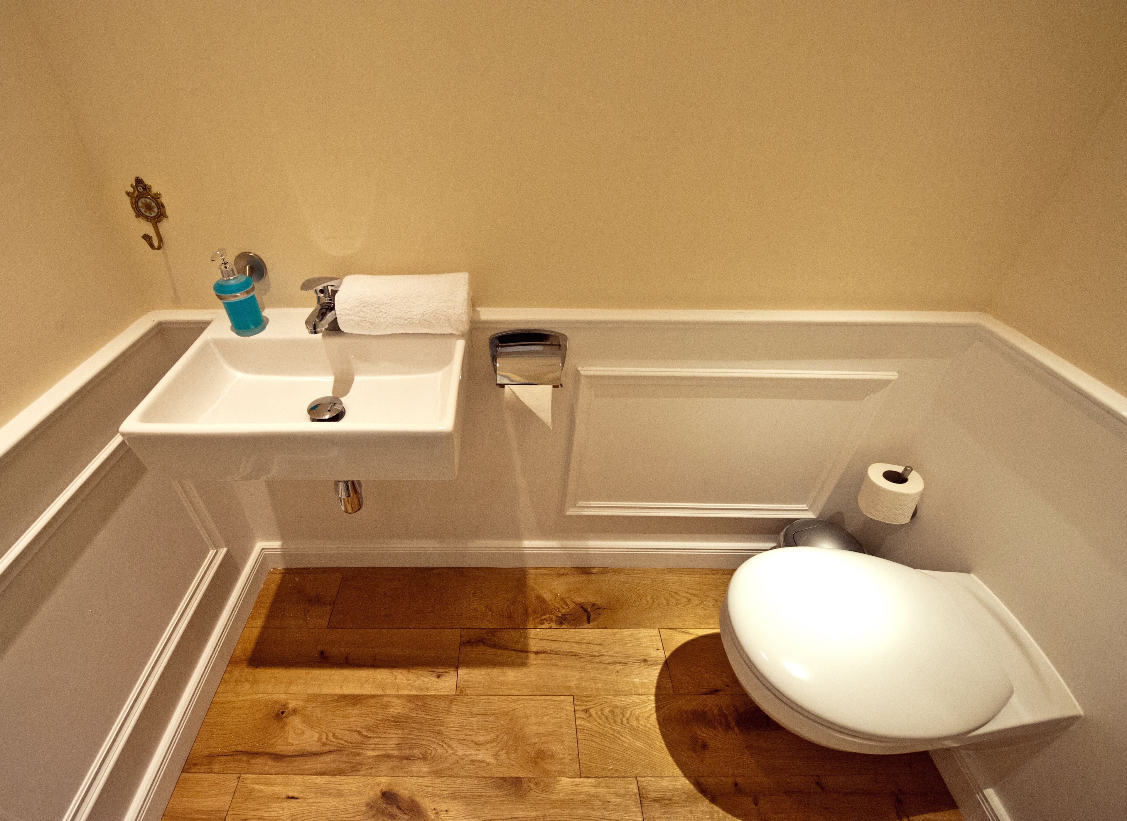 A bathroom with a wooden floor, a white sink, a toilet, and a towel hanging on the wall.