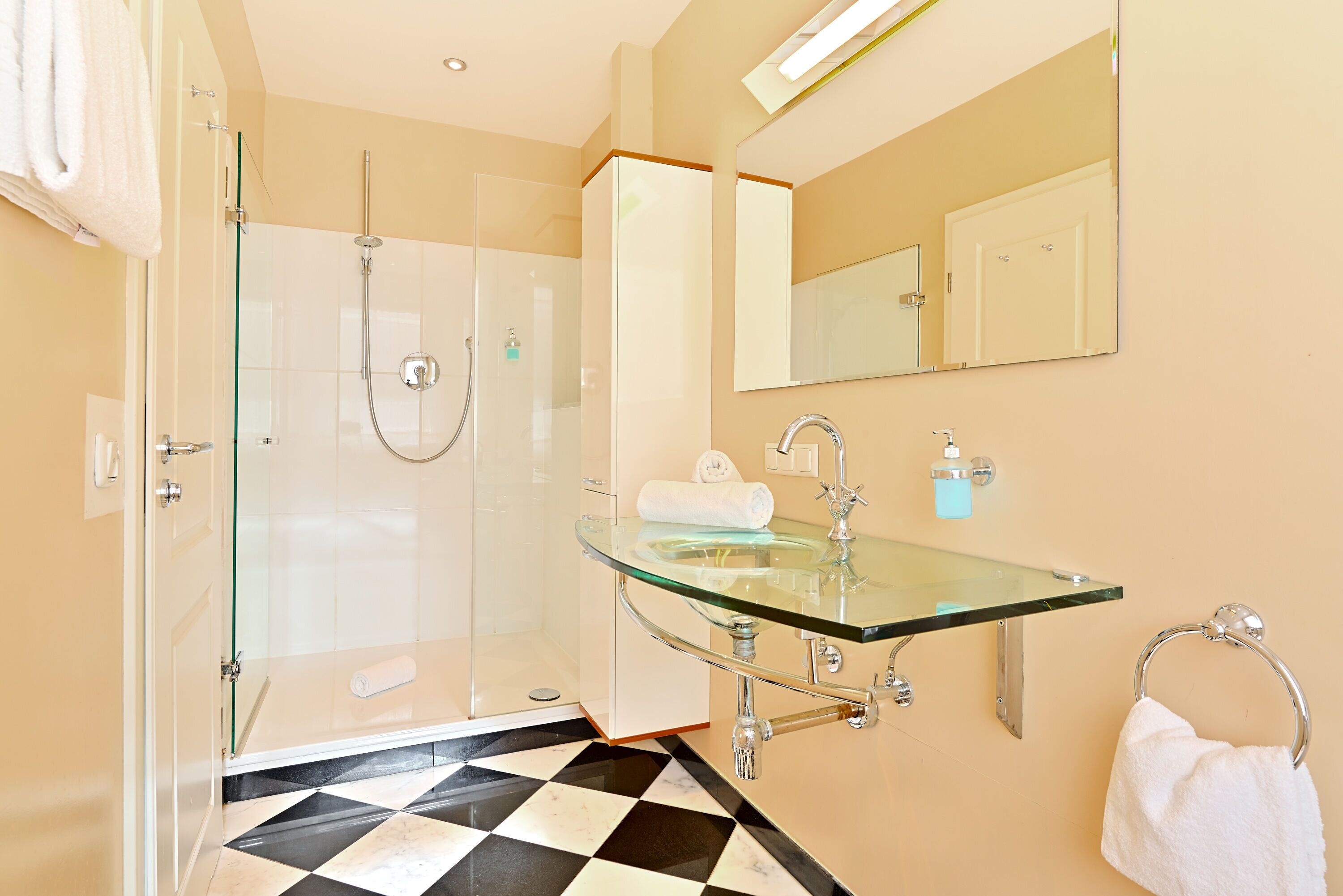 A modern bathroom with a glass shower enclosure, a glass sink, and a large mirror.