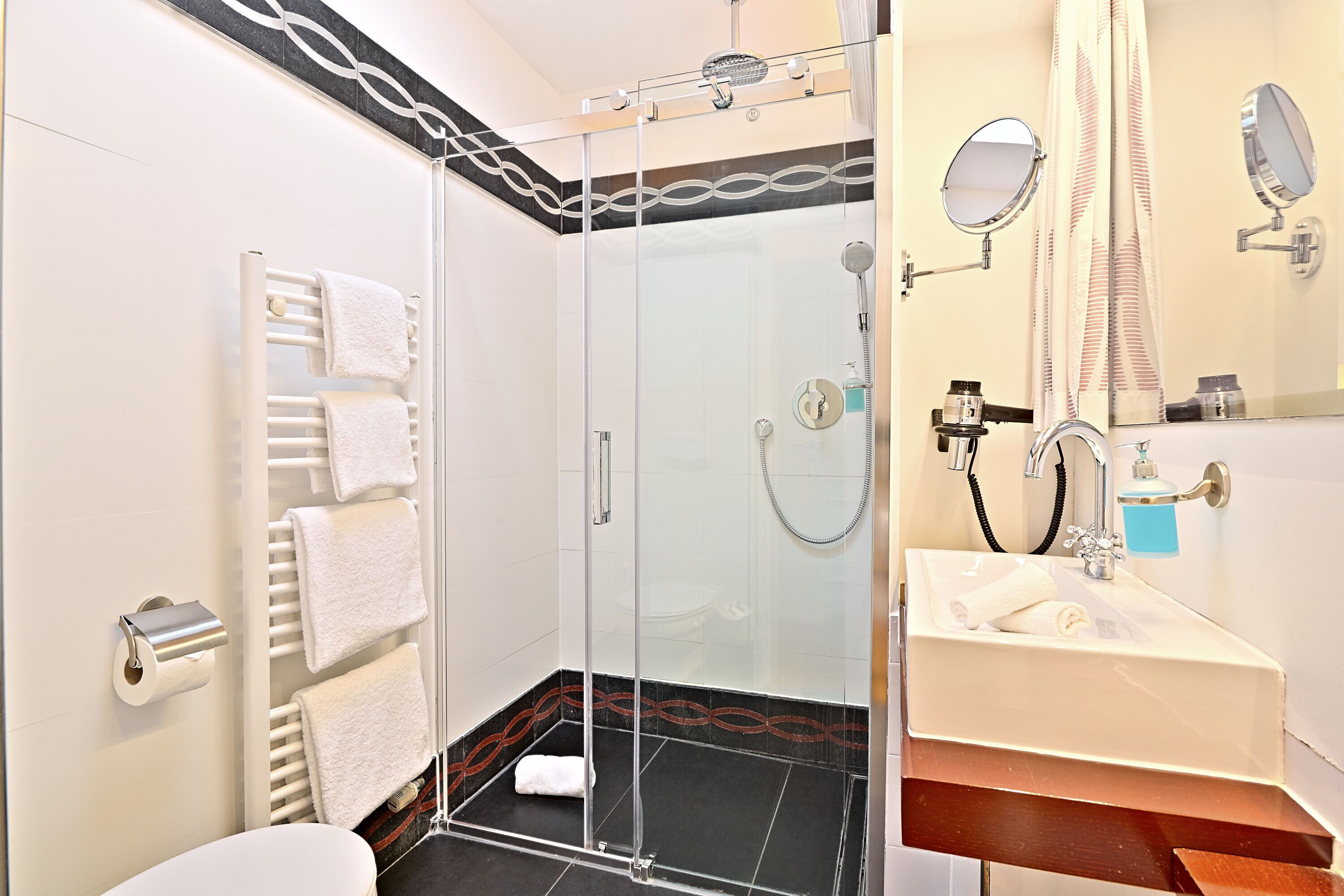 Een moderne badkamer met een douchecabine van glas, een witte wastafel met spiegel, en een handdoekrek met meerdere handdoeken.