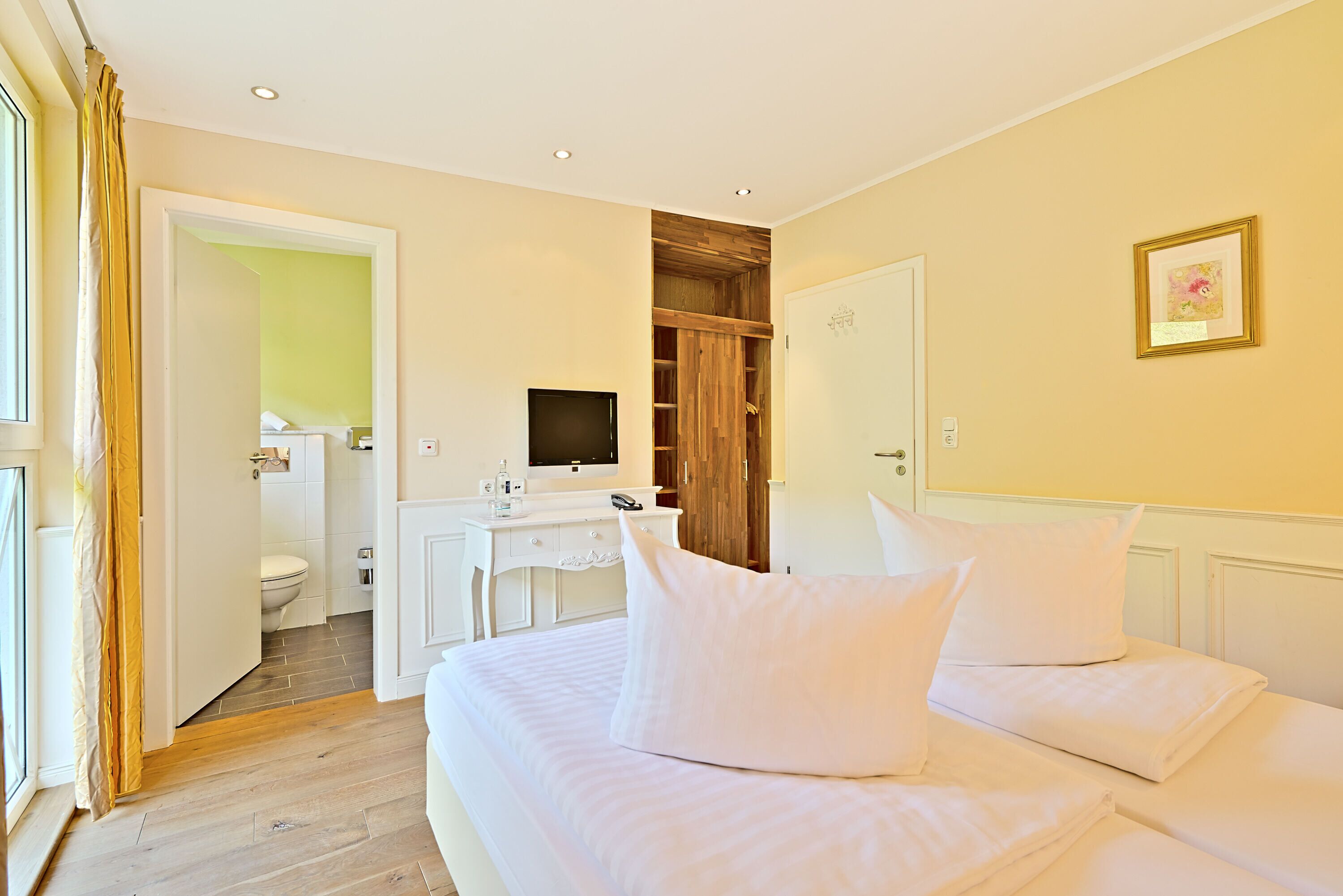 A hotel room with a bed, a desk, a television, and a bathroom visible through an open door.