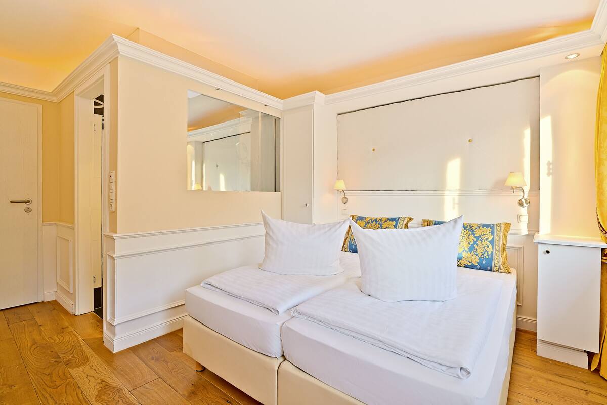 Un lit double avec du linge de lit blanc, une table de chevet, un miroir et une armoire.