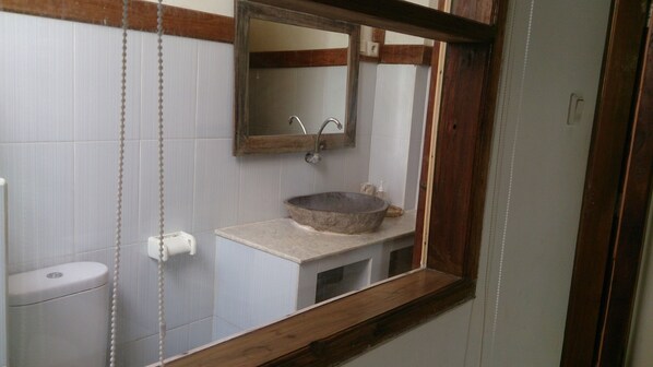 A bathroom with a wooden-framed mirror, a stone basin sink, and a toilet. - Rumah Purnama (Gili Trawangan)
