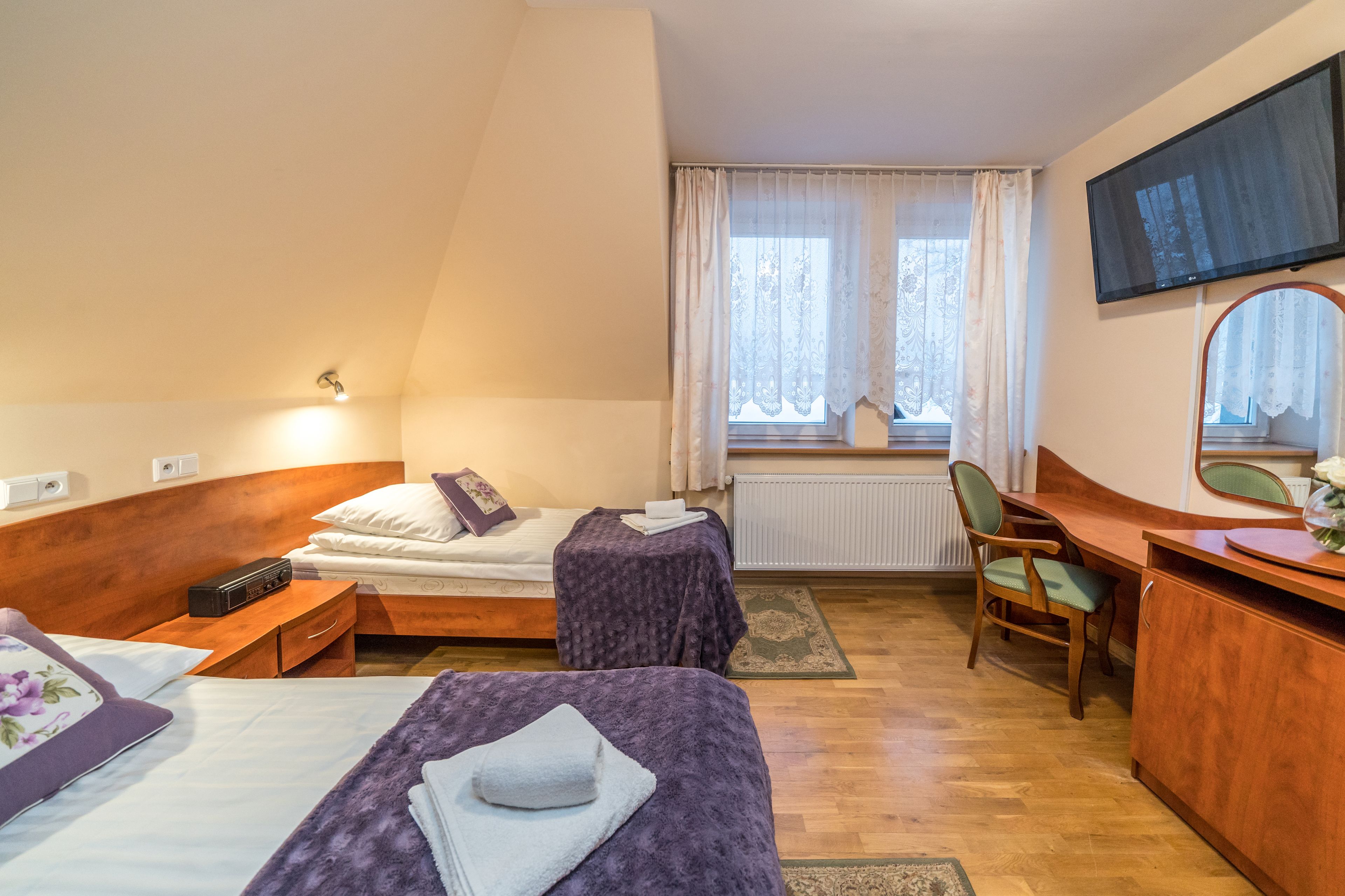 Une chambre d’hôtel avec deux lits, un bureau, une chaise, une télévision et une fenêtre avec des rideaux.