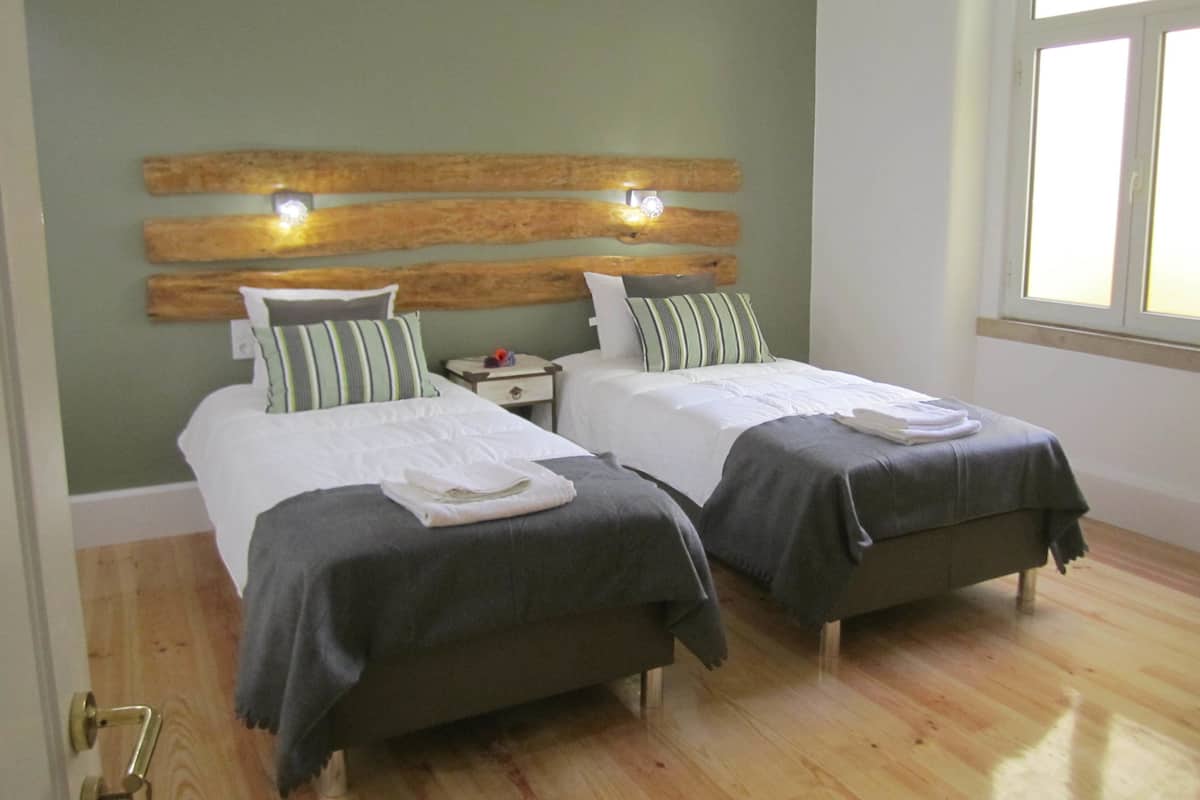 A room with two beds, wooden headboard, bedside tables, and a window.