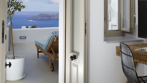Ein Zimmer mit Balkon, einem Holzsessel, einer Topfpflanze, einem Schreibtisch mit Stuhl und einem großen Fenster mit Meer- und Landschaftsblick.