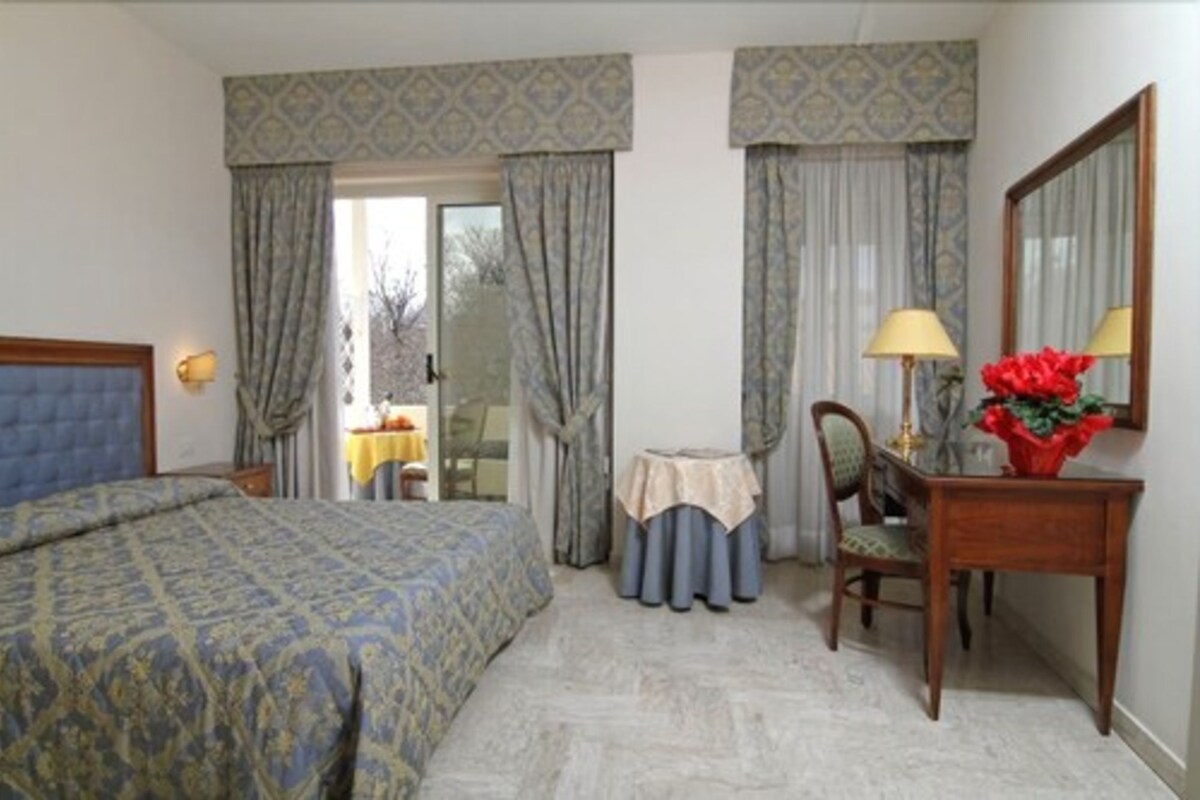 Una habitación de hotel con una cama, un escritorio con silla, una mesita y un espejo.