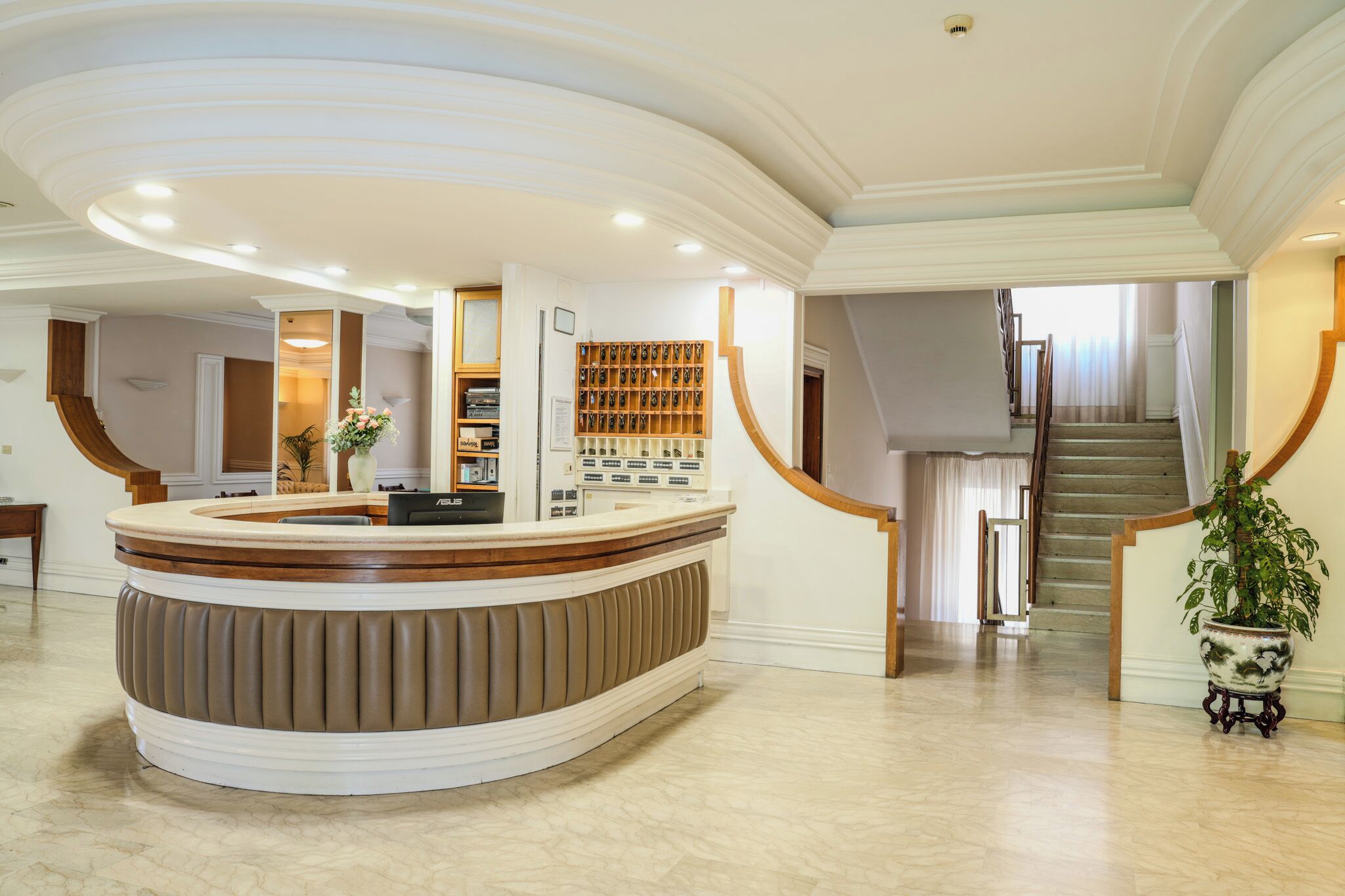 A reception area with a curved counter, a staircase, and a potted plant.