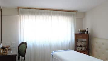 Ein Zimmer mit einem Bett, einem Sessel, einem Tisch mit Schüssel und Glas sowie einem Holzschrank mit Handtüchern.