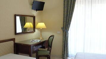 Ein Hotelzimmer mit zwei Betten, einem Schreibtisch mit Stuhl, einem an der Wand befestigten Fernseher und einem Fenster mit Vorhängen.