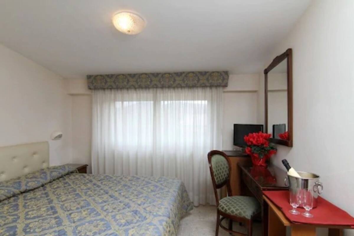 Un dormitorio con una cama, un escritorio con una computadora, una silla y un espejo.