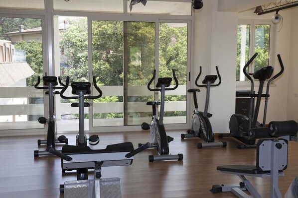 Een fitnessruimte met diverse trainingsapparaten, grote ramen en uitzicht op groen buiten.