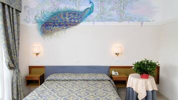 A hotel room with a large peacock mural on the ceiling, a bed with patterned bedding, bedside lamps, a nightstand, a small table with a plant, and a telephone.