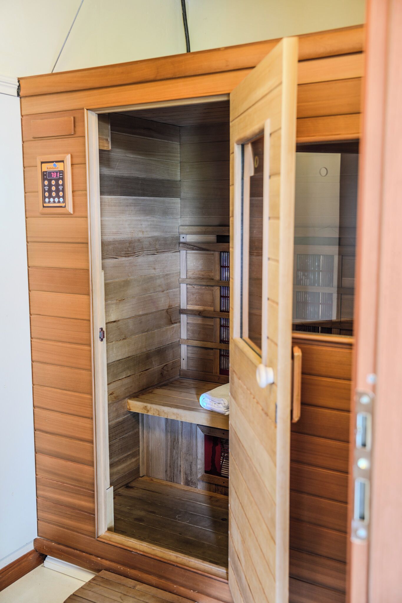 A sauna with a wooden exterior, a control panel, and a bench inside.
