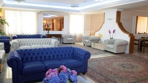 Amplia sala de estar con un sofá azul, sillones blancos y un tapete estampado.