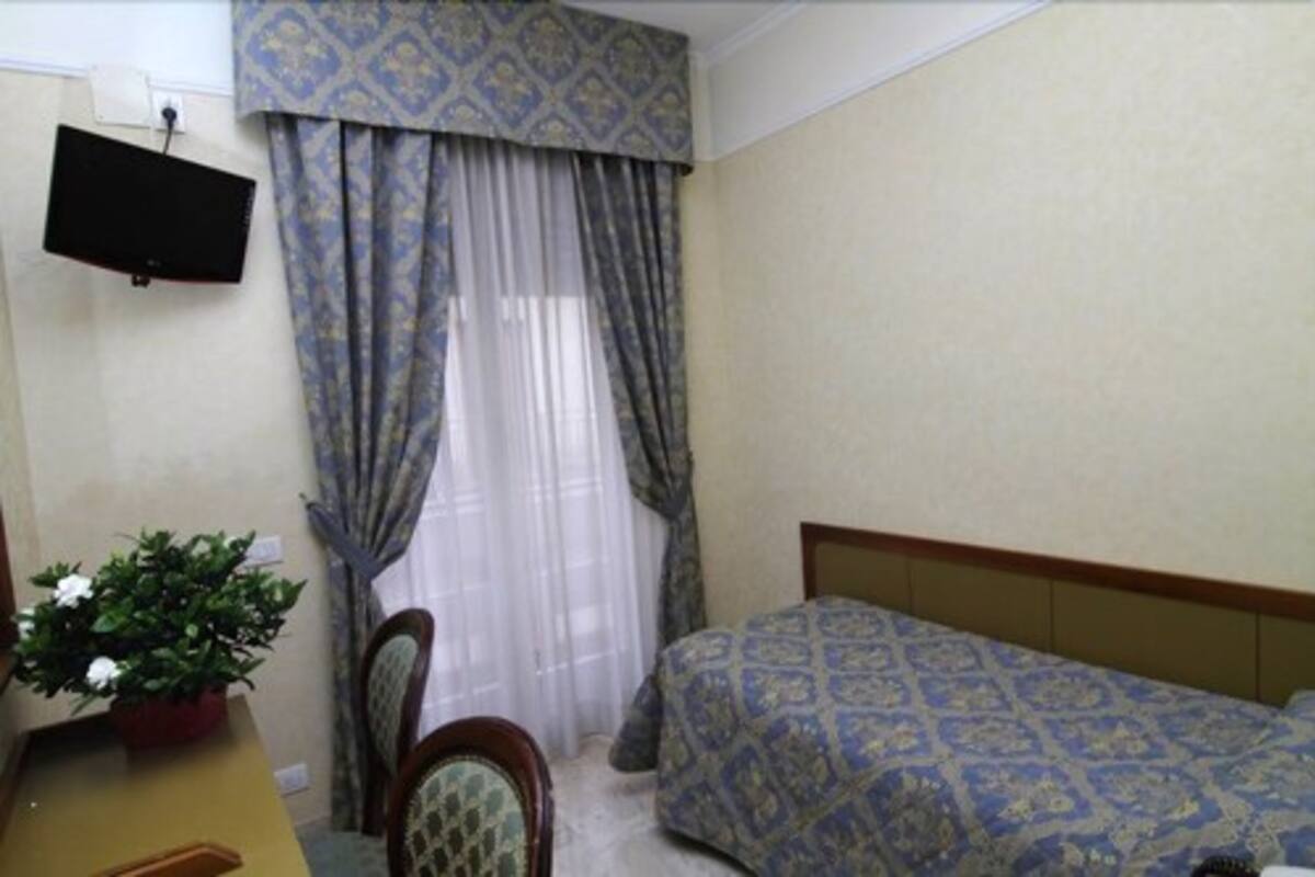 Un dormitorio con cama, una silla, un escritorio con planta y televisor montado en la pared.
